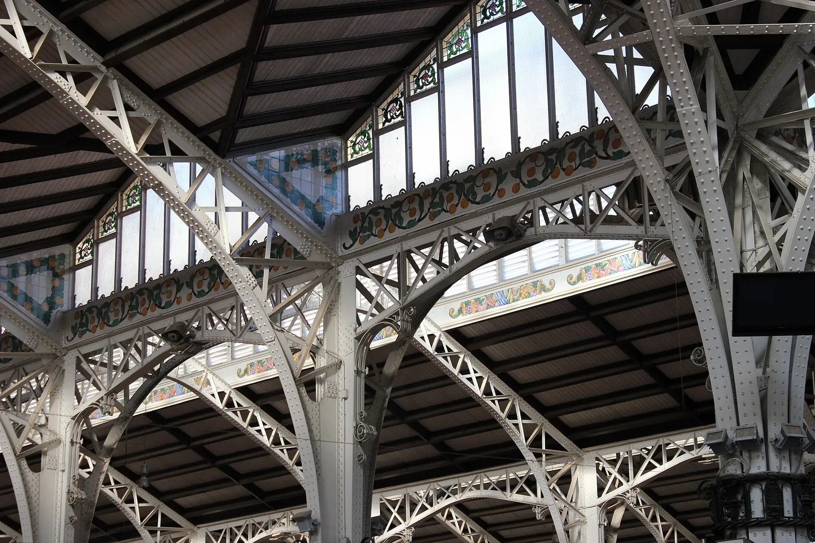 The riveted iron frame and tiled frieze under the glazed roof of the Mercado Central in Valencia